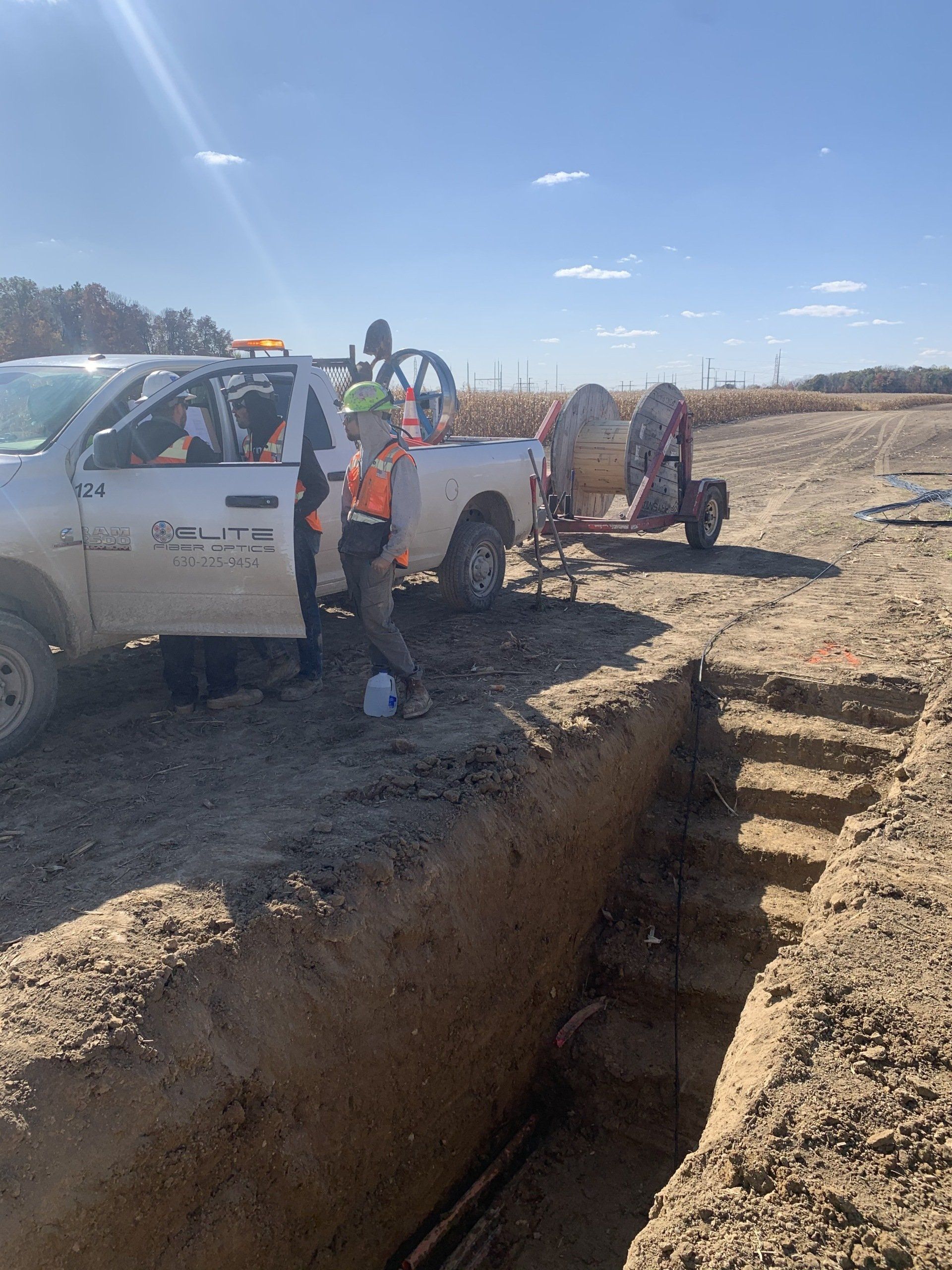 A white truck is parked in the dirt next to a trench.