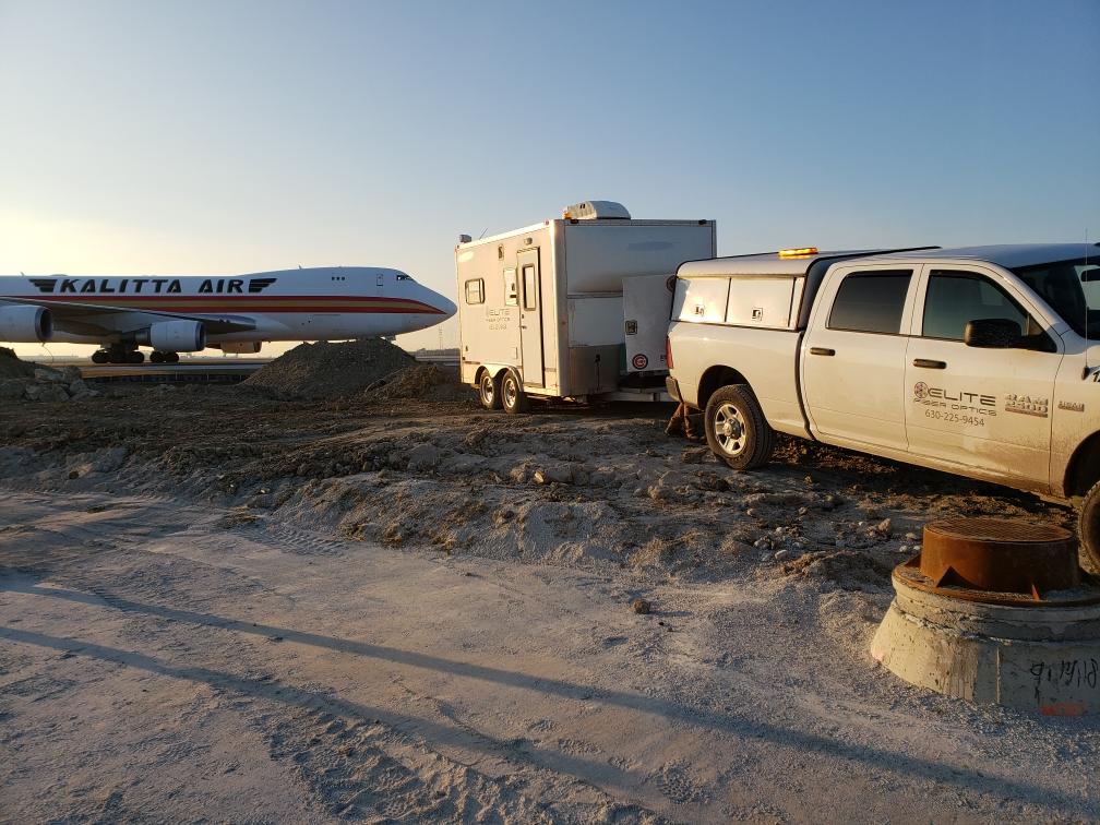 A truck is towing a trailer with an airplane in the background.