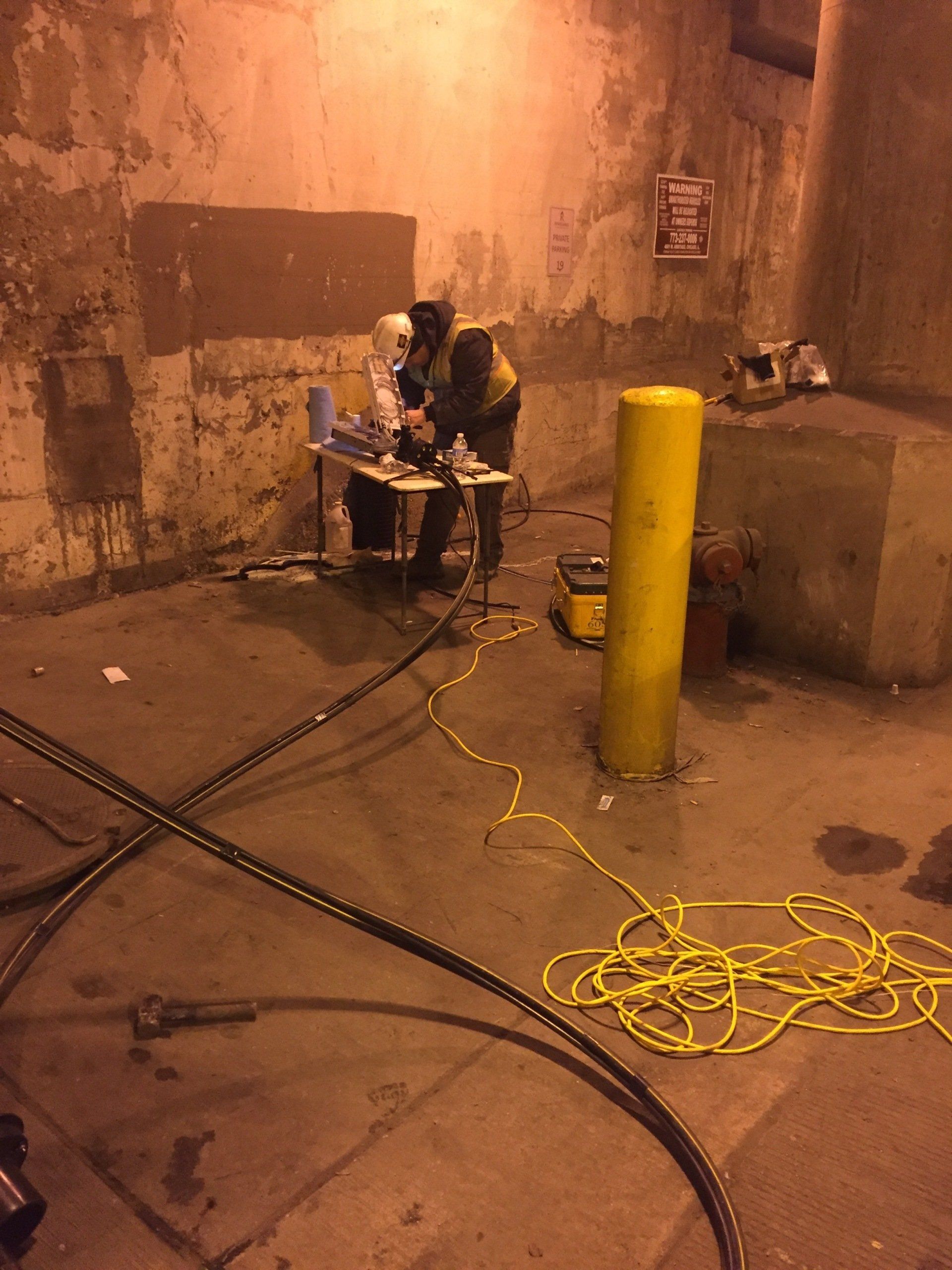 A man is sitting at a table in a dark room next to a yellow pole.