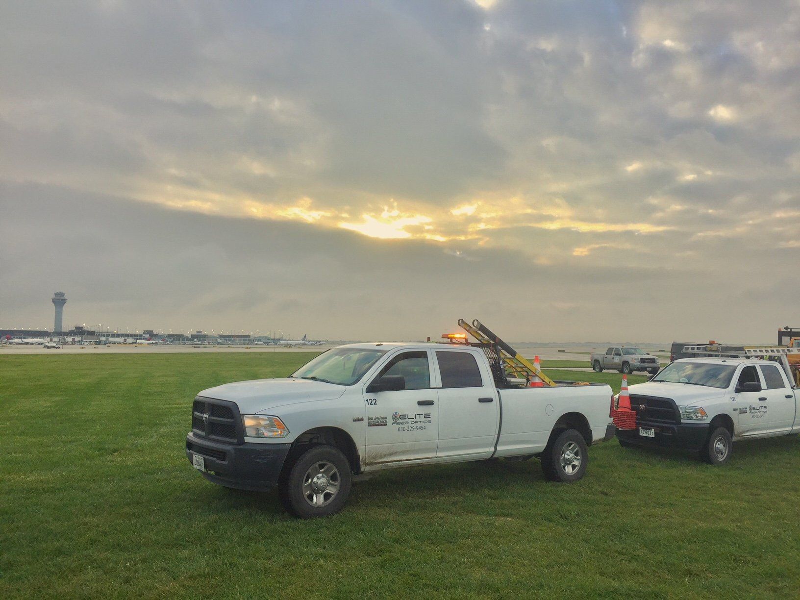 Two white trucks are parked in a grassy field.