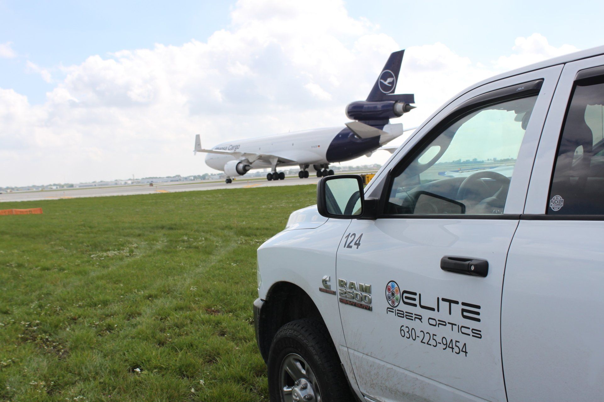 A white truck is parked in front of an airplane on a runway.
