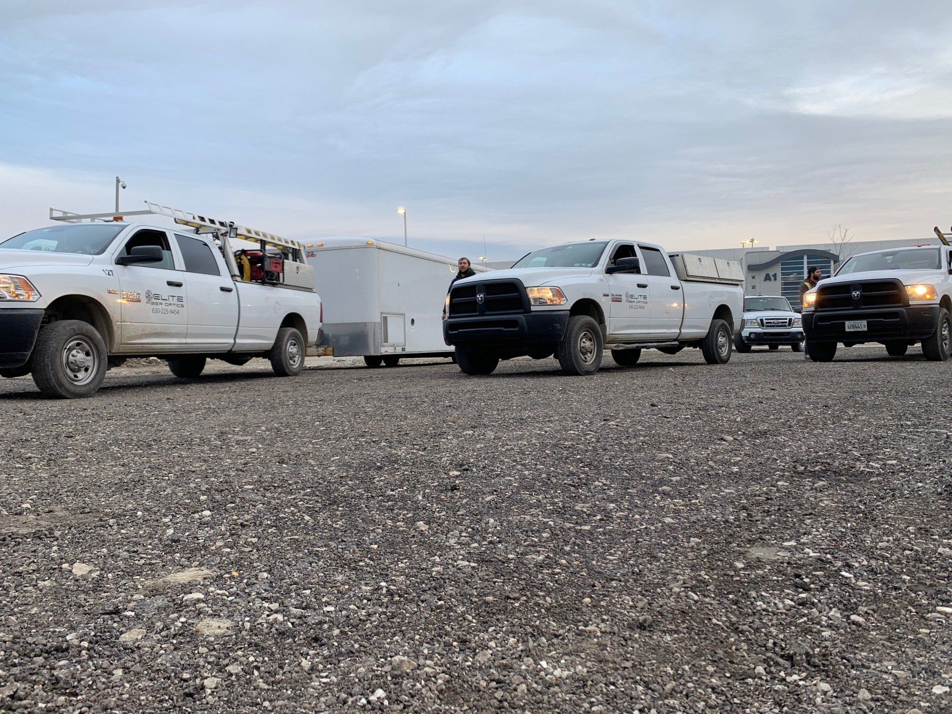 A row of trucks are parked in a gravel lot.