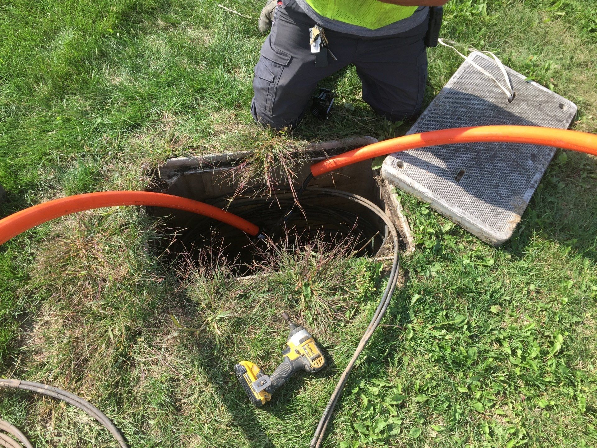 A man is kneeling down in the grass next to a drill.