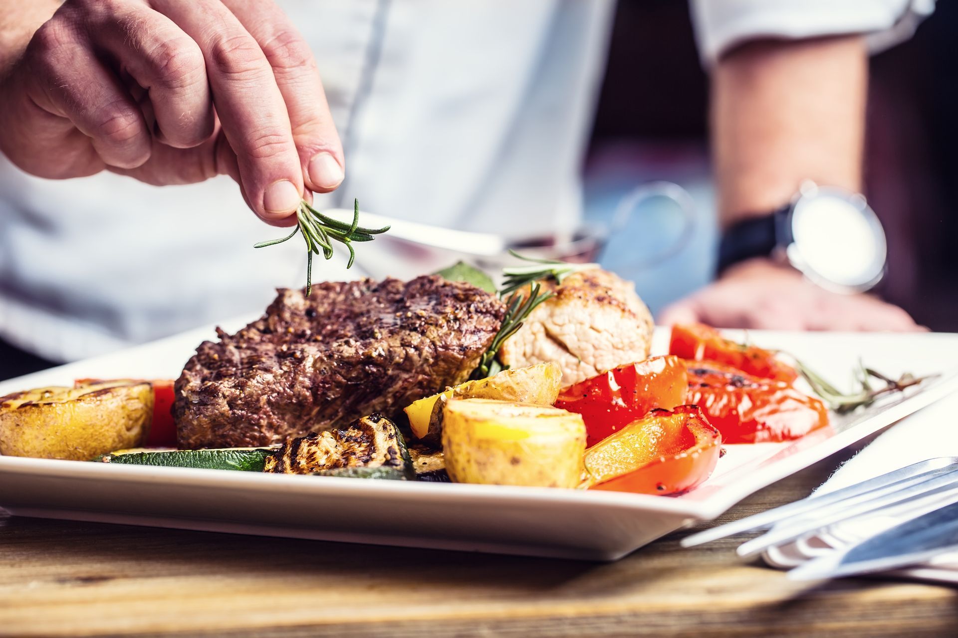 A person is cutting a piece of meat on a plate with vegetables.