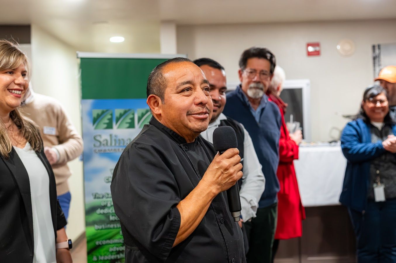 A man is talking into a microphone while standing in front of a group of people.