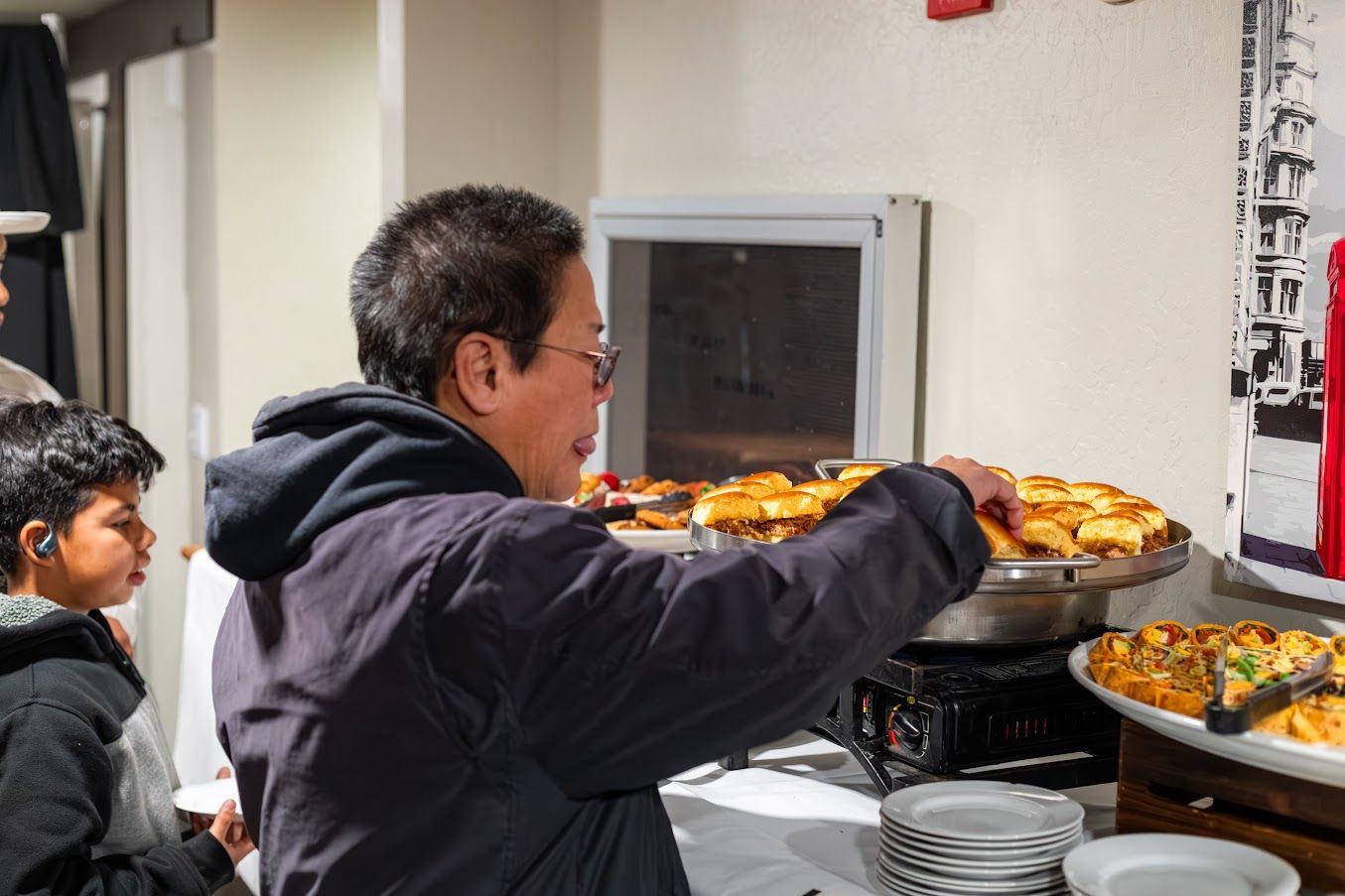 A woman is reaching for a plate of food at a buffet table.