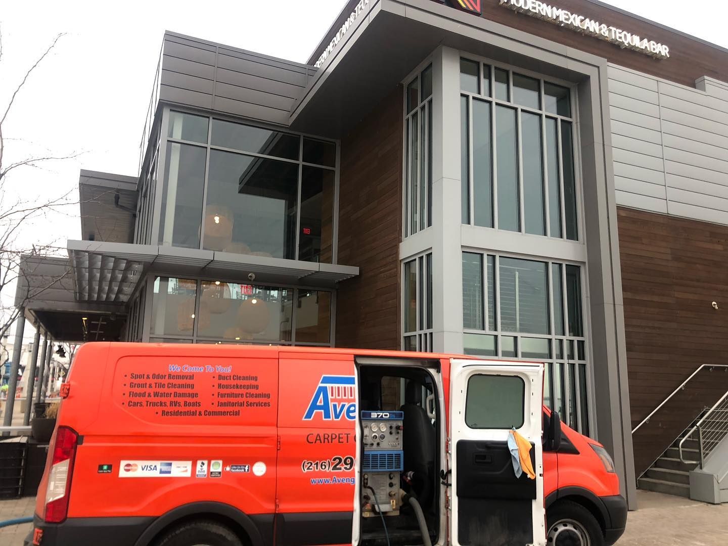 An orange van is parked in front of a building.