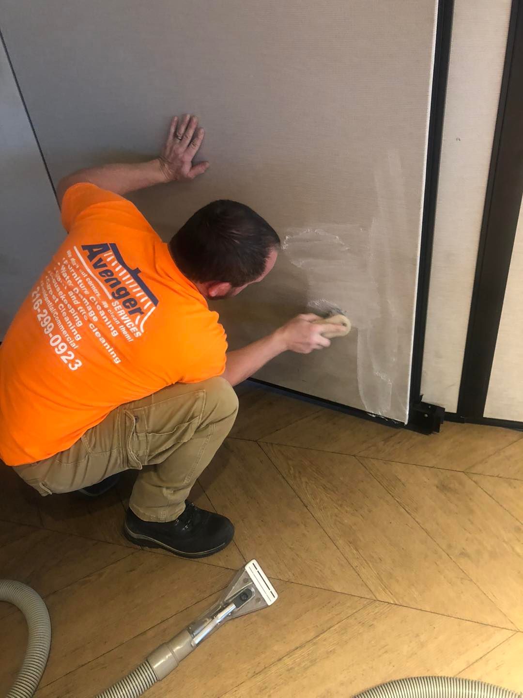 A man in an orange shirt is cleaning a wall with a vacuum cleaner.