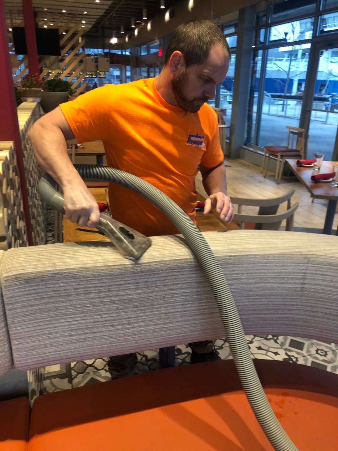A man is using a vacuum cleaner to clean a couch in a restaurant
