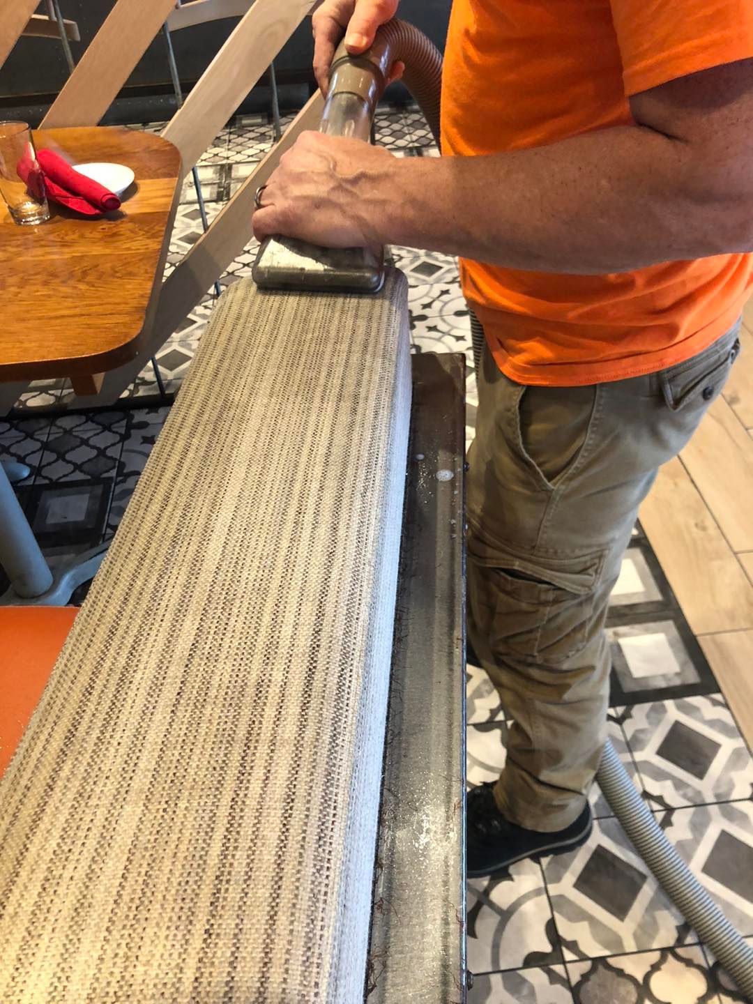 A man in an orange shirt is cutting a piece of wood with a saw.