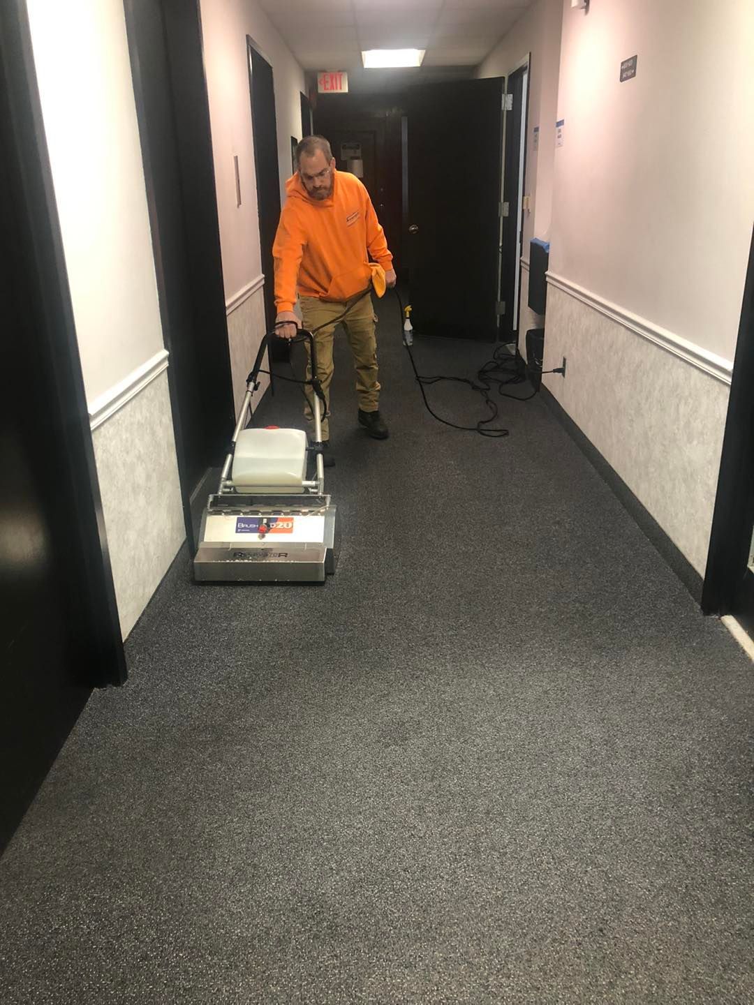 A man is cleaning the carpet in a hallway with a machine.