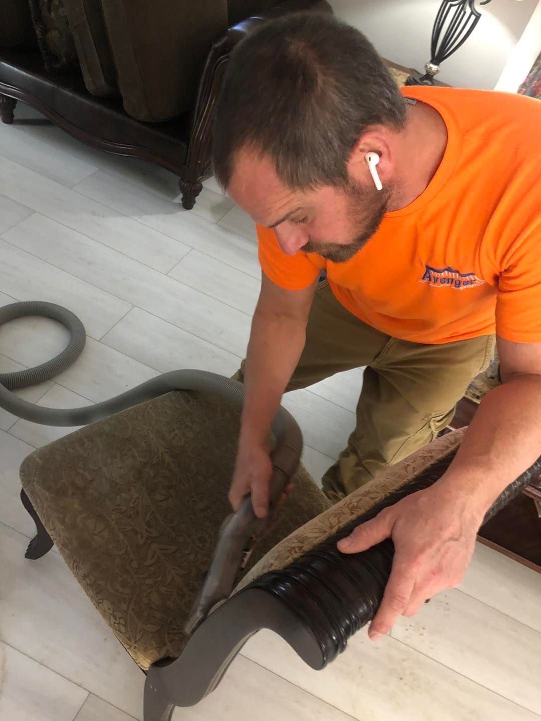 A man is cleaning a chair with a vacuum cleaner.