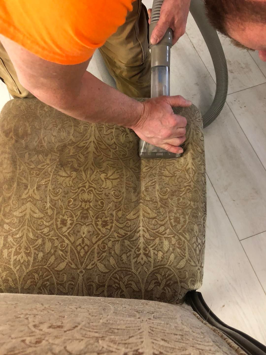 A man is cleaning a chair with a vacuum cleaner.