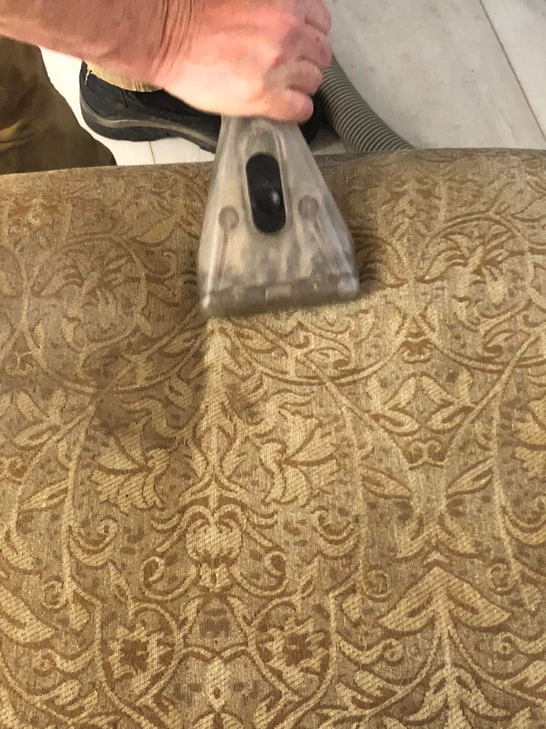 A person is cleaning a couch with a vacuum cleaner.