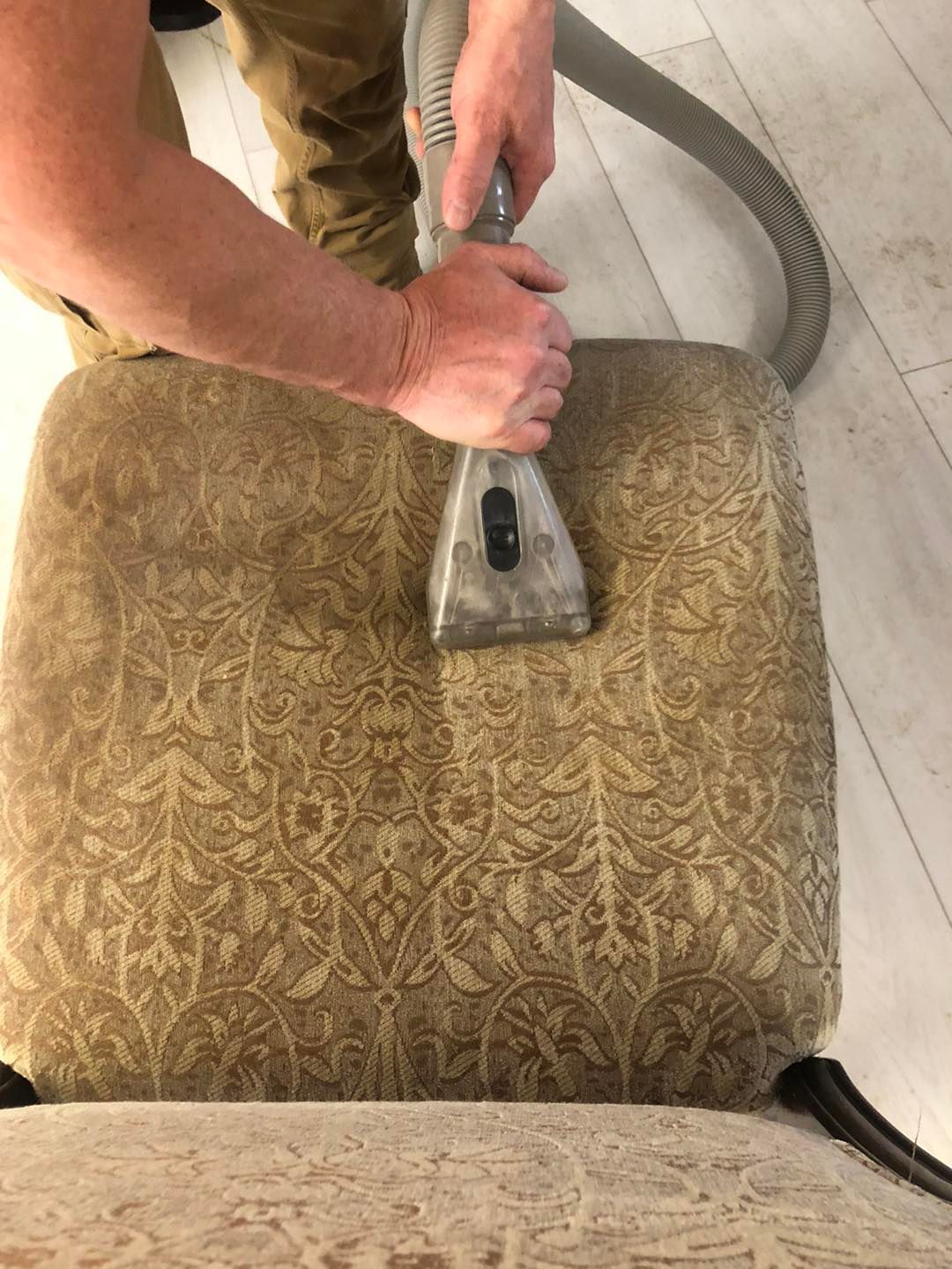 A person is cleaning a chair with a vacuum cleaner.