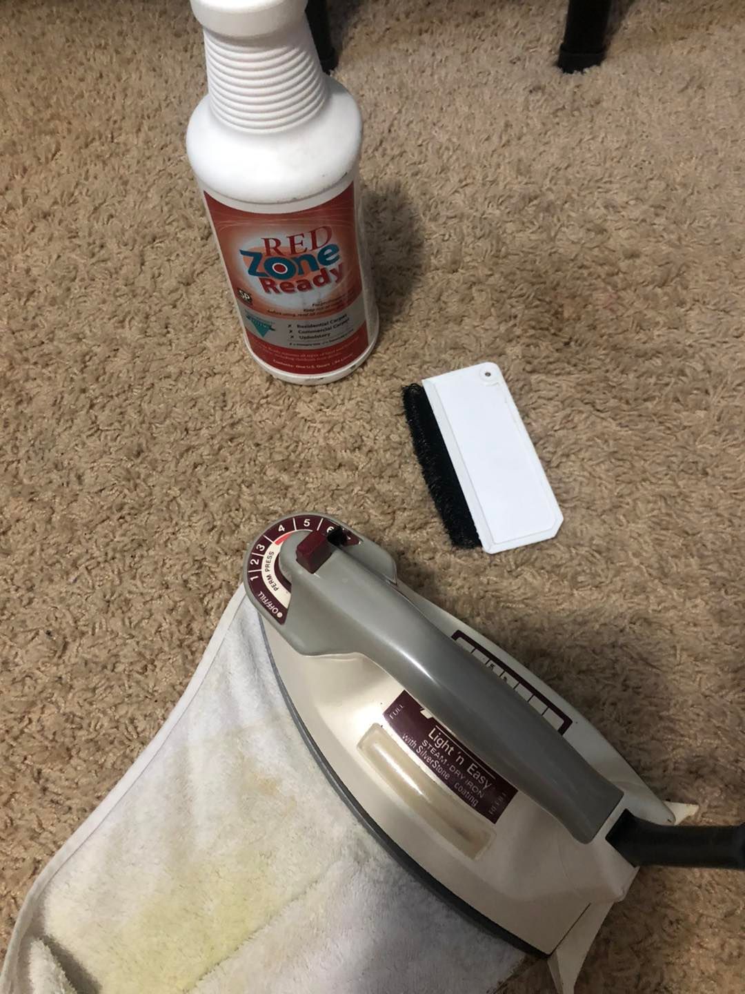 An iron is sitting on a towel next to a bottle of cleaner and a brush.
