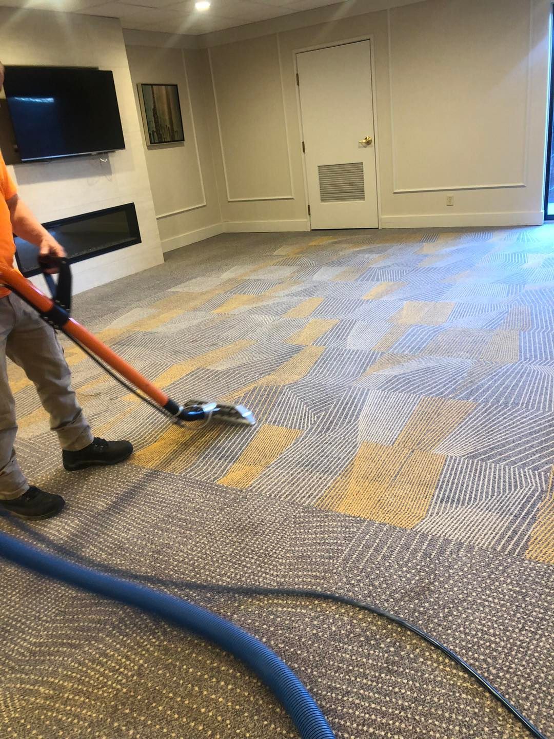 A man is cleaning a carpet with a vacuum cleaner in a room.