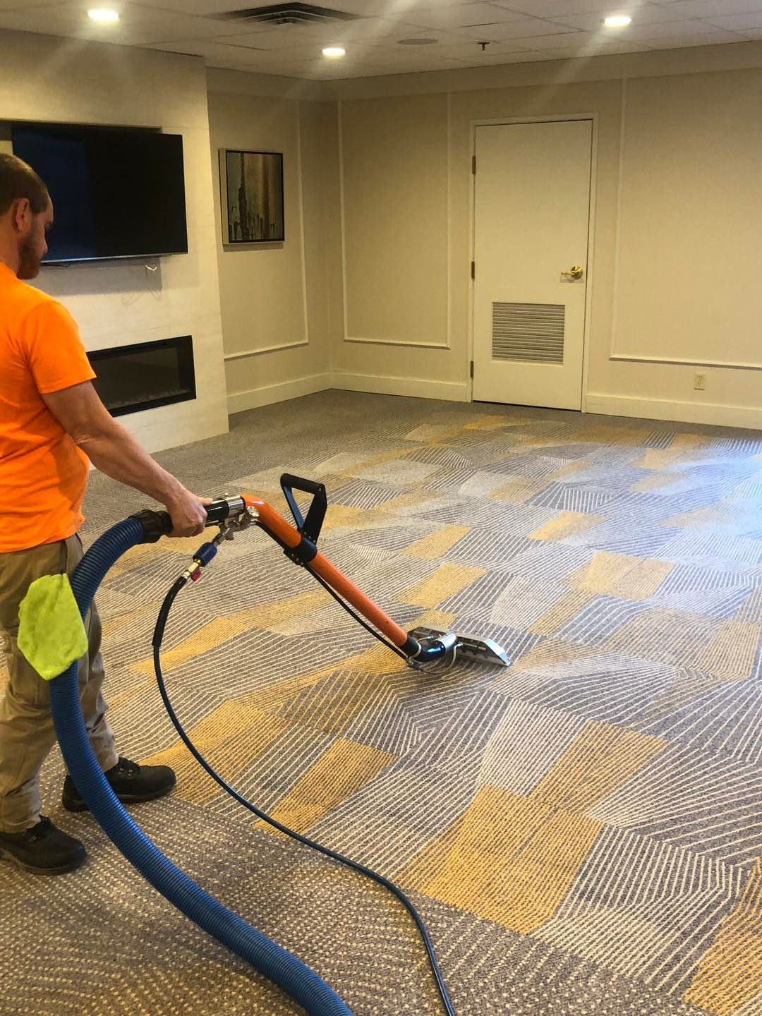 a man in an orange shirt is using a vacuum cleaner to clean a carpet