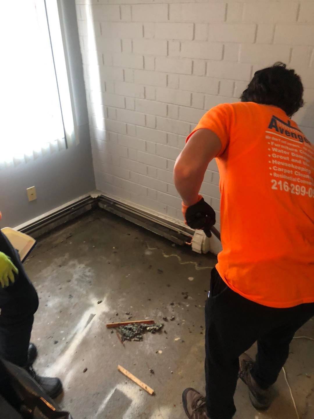 A man in an orange shirt is cleaning the floor of a room.