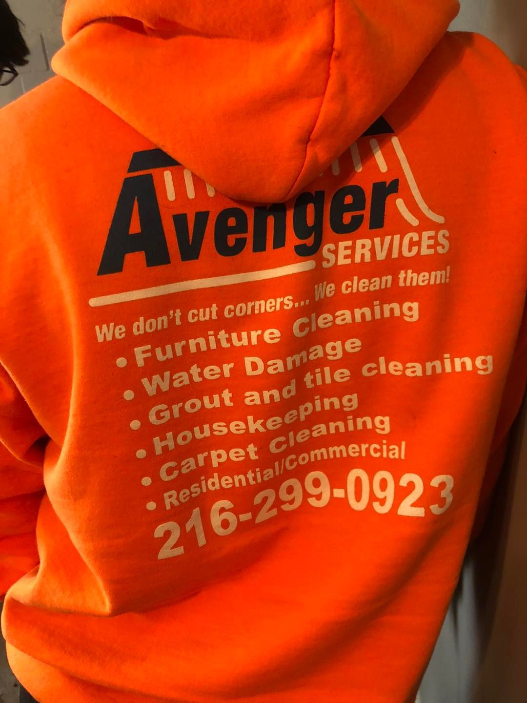 A person wearing an orange hoodie that says avenger services
