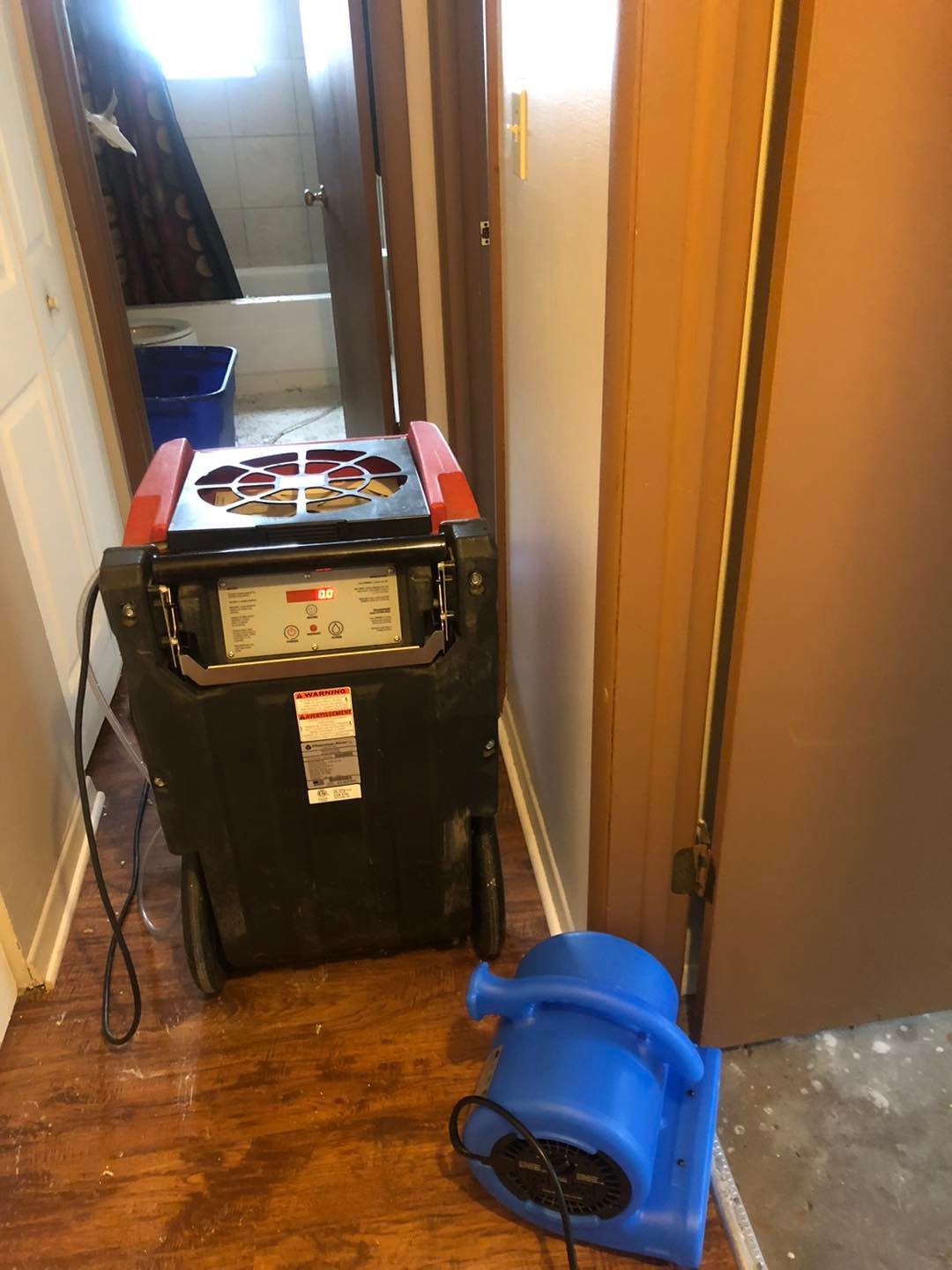 A machine is sitting on the floor in a hallway next to a blue fan.