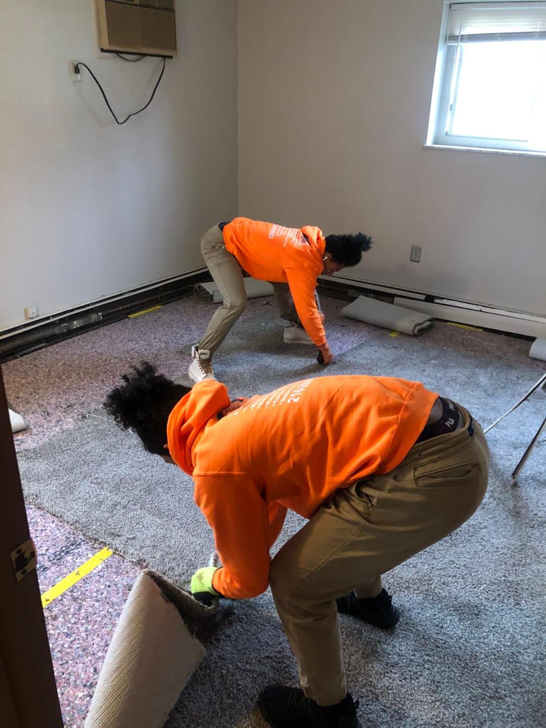 Two people are laying carpet in a room.