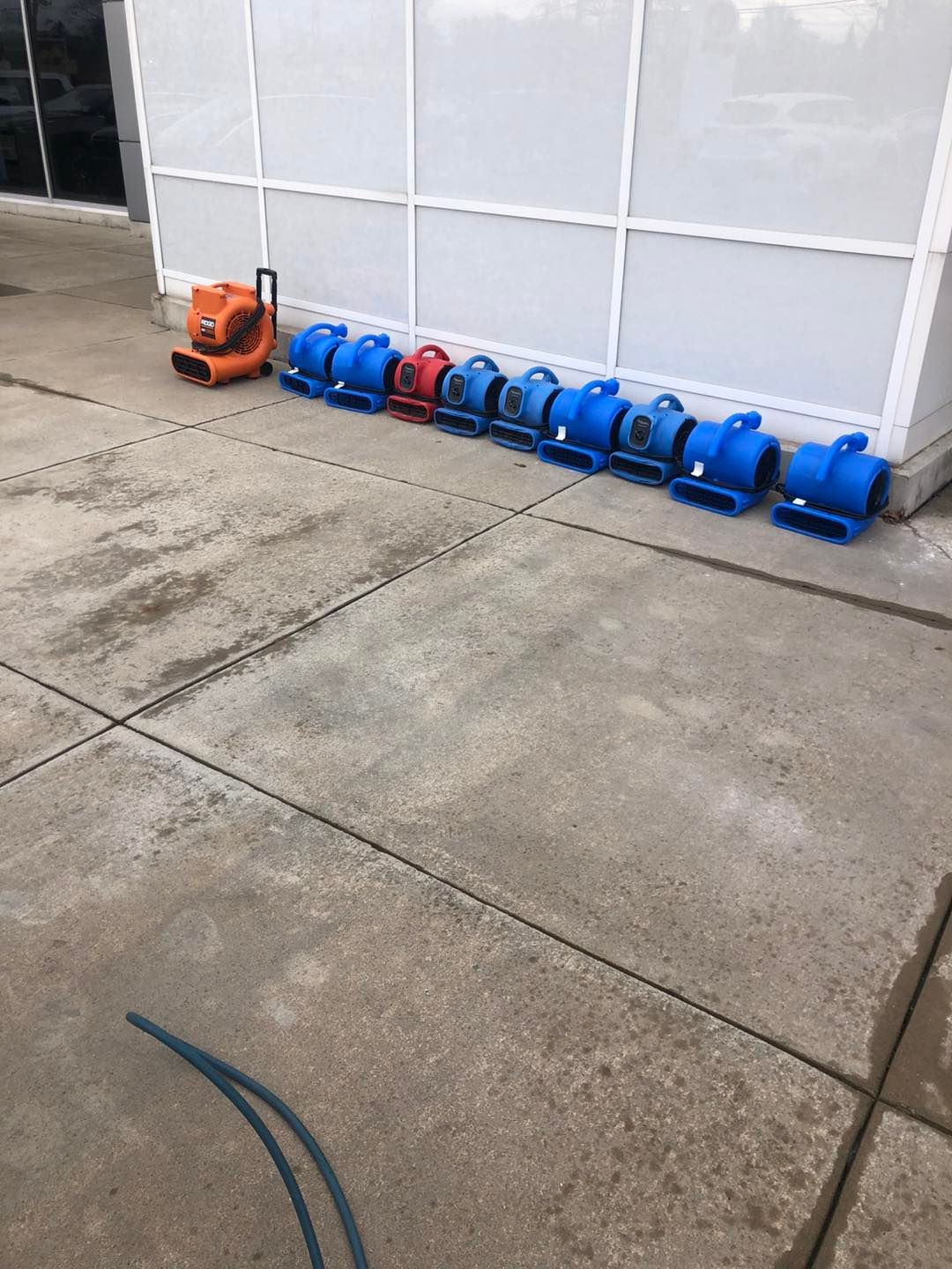A row of blue and orange air conditioners are lined up on a sidewalk.