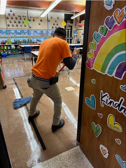 A man is mopping the floor of a classroom with a mop