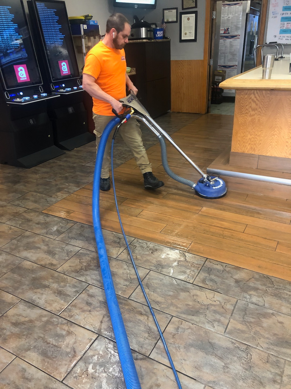 A man in an orange shirt is using a vacuum cleaner on a tiled floor
