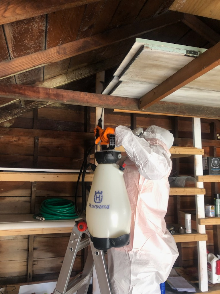 A man in a protective suit is spraying a ceiling in a garage.