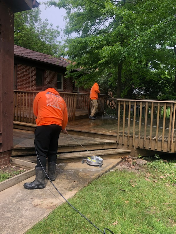 Two men are cleaning a deck in front of a brick house