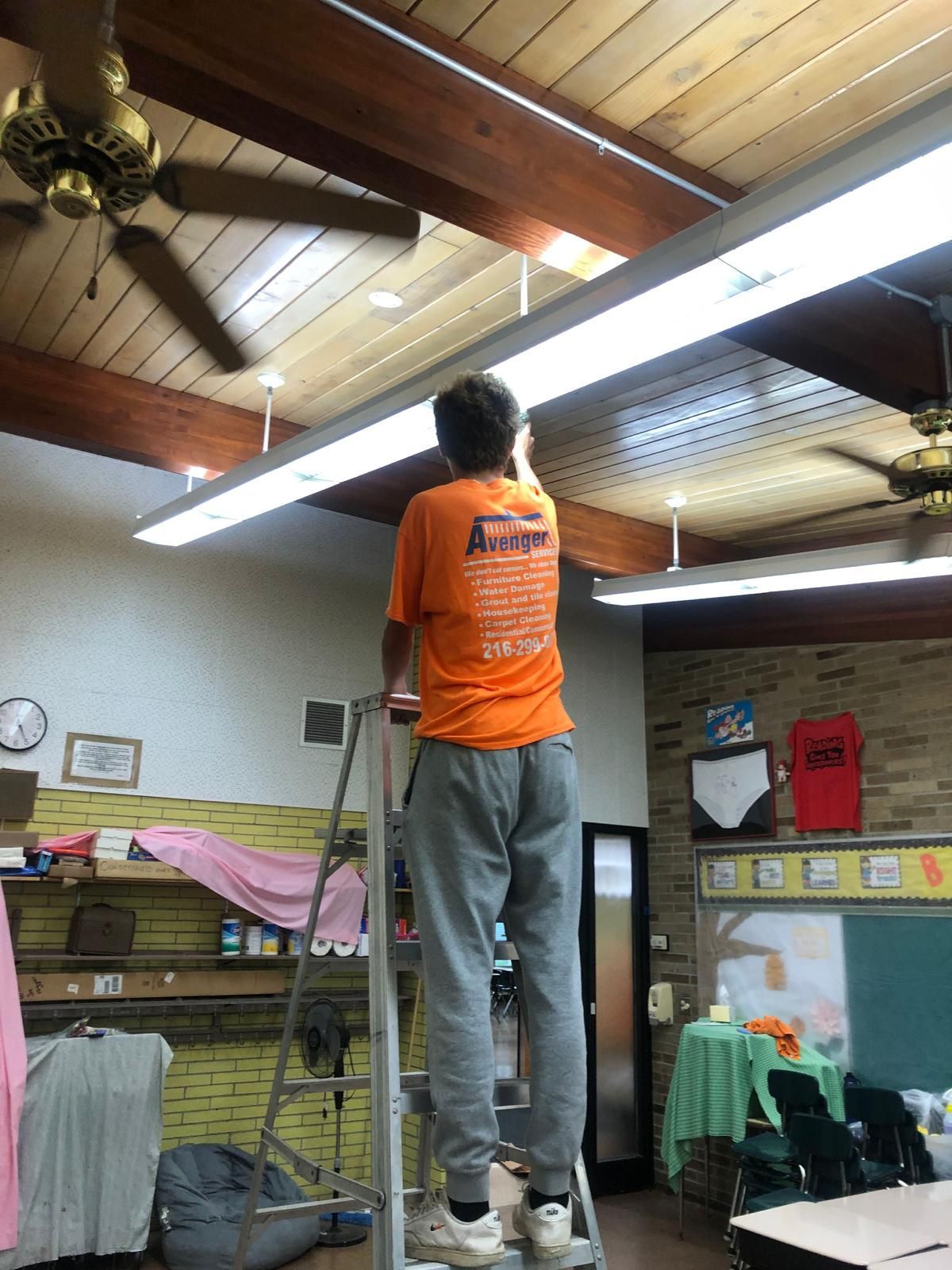 A man on a ladder wearing an orange shirt that says avengers