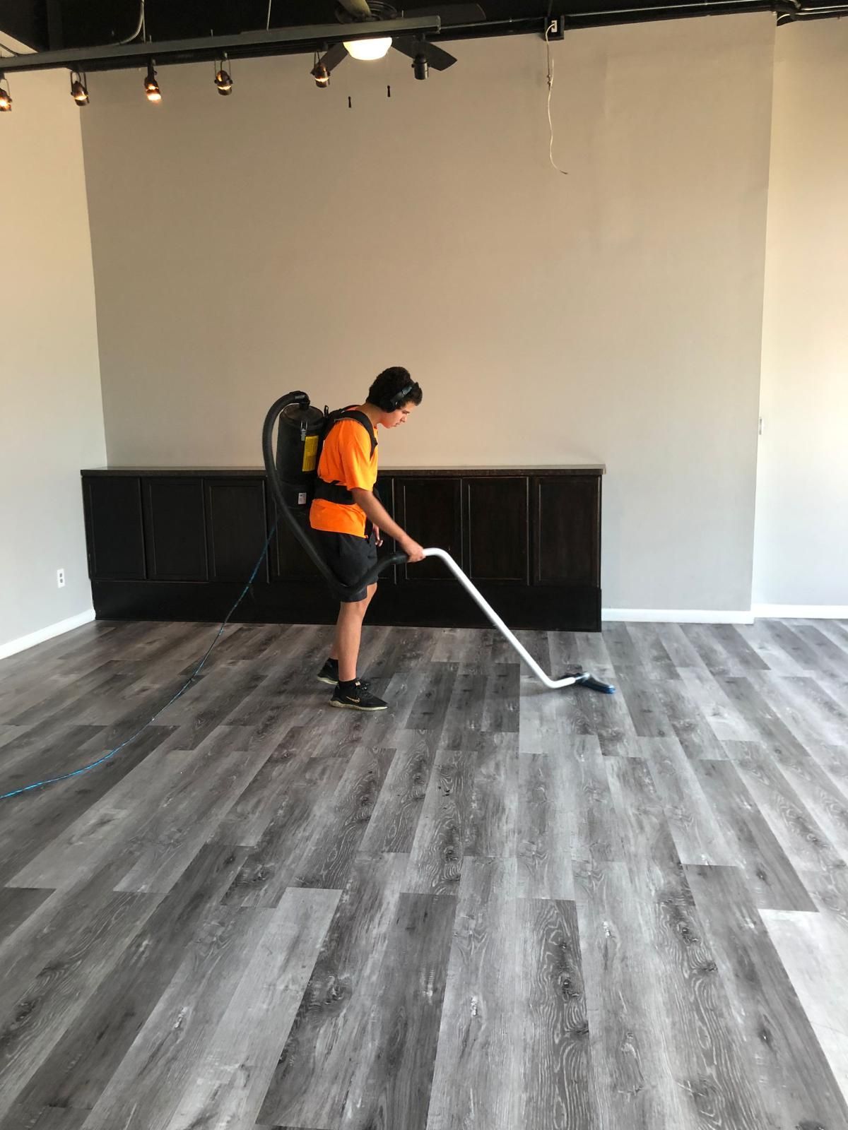 A man wearing an orange shirt is vacuuming the floor