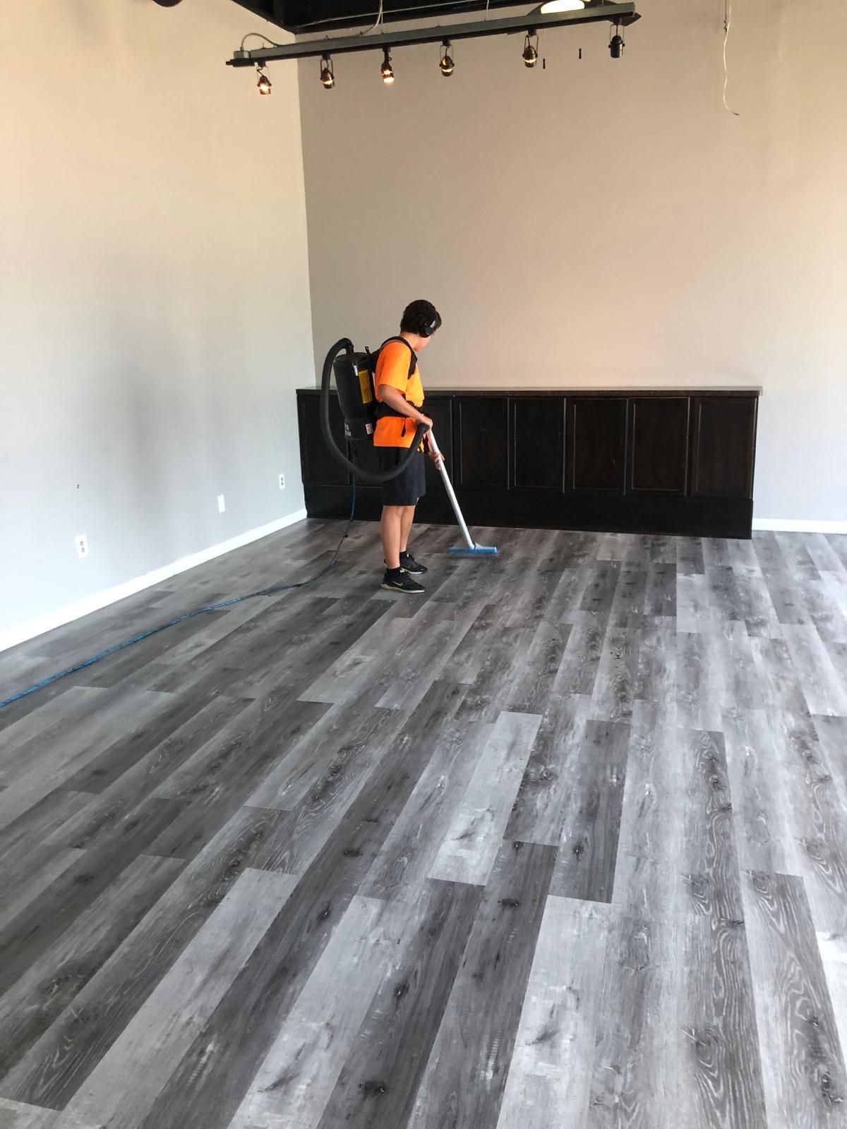 A man is using a vacuum cleaner to clean a wooden floor