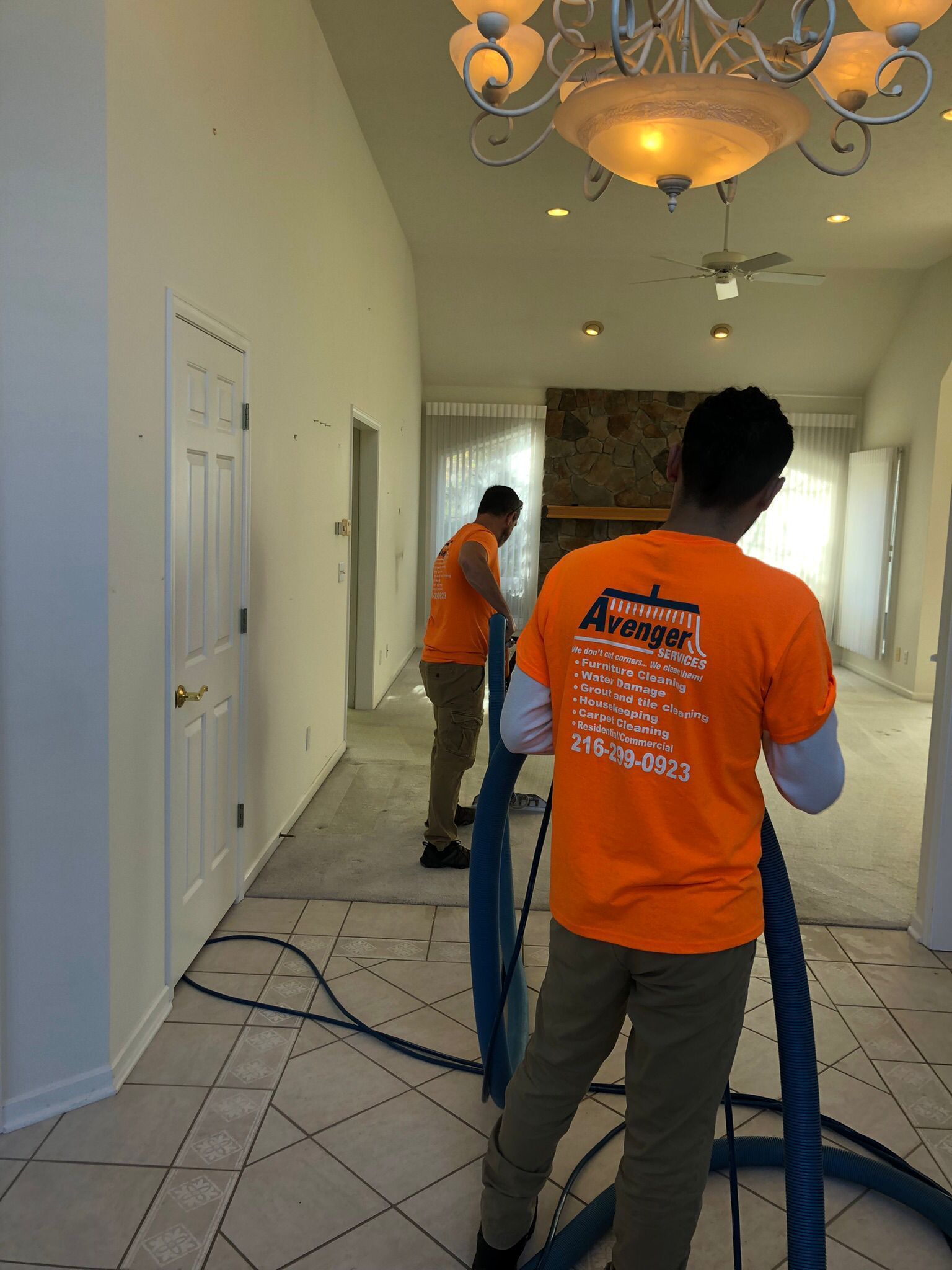 Two men in orange shirts are cleaning a tiled floor