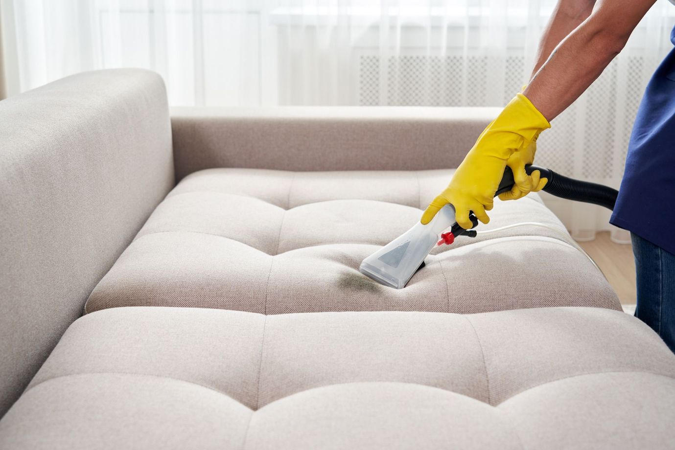 A person wearing yellow gloves is cleaning a couch