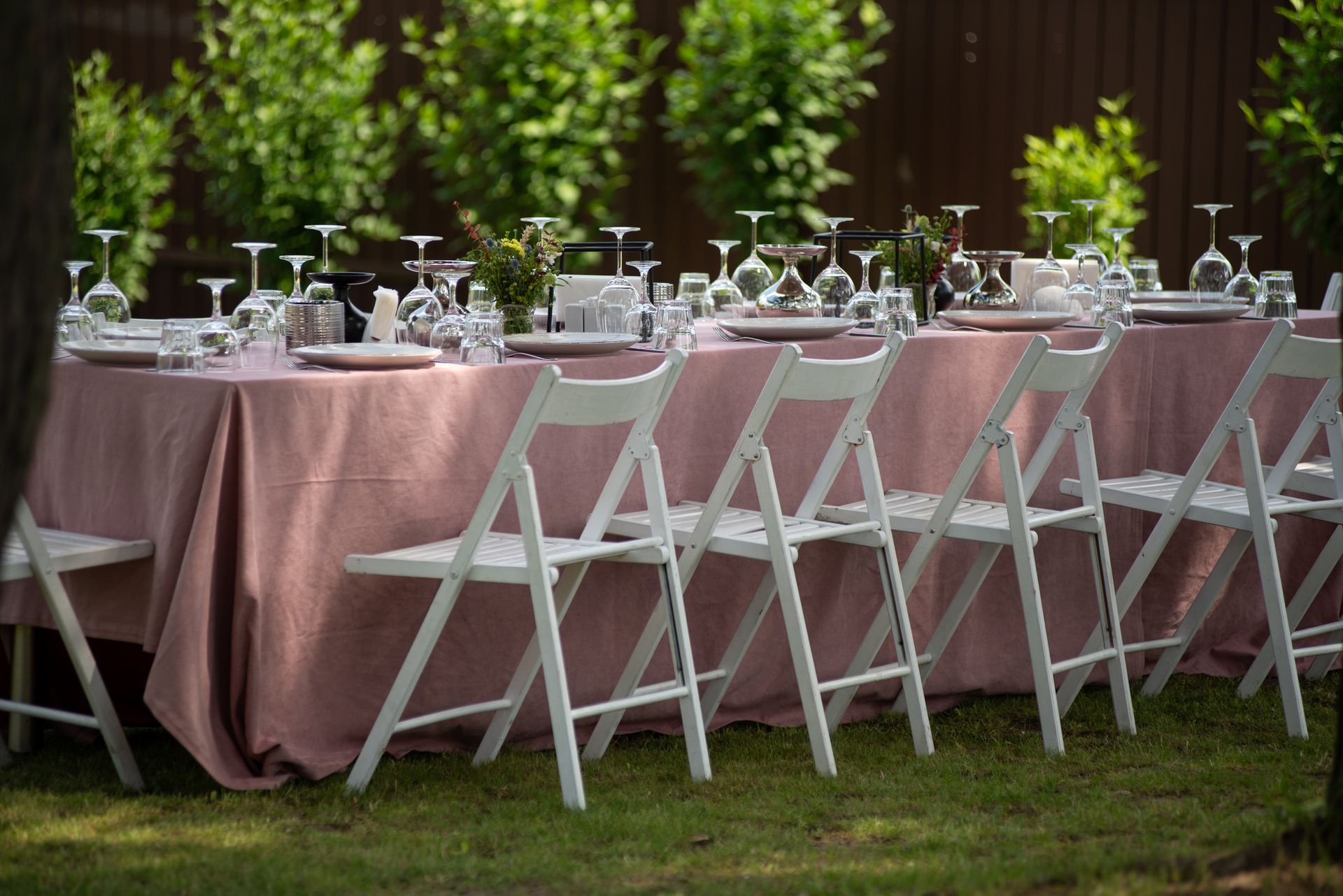 A long table with a pink tablecloth and white folding chairs.