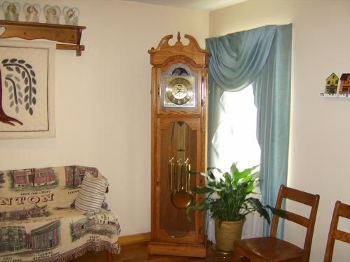 Grandfather clock next to a window with blue curtains. Living room with a sofa and chairs.