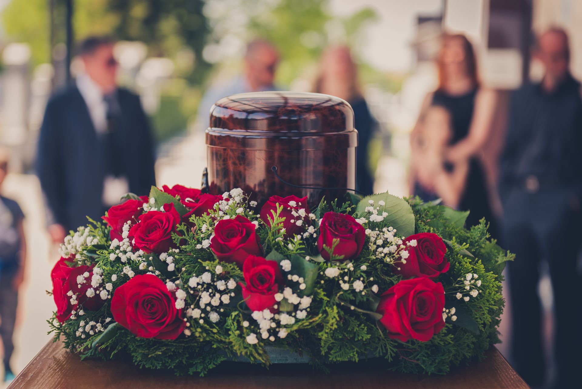 Urn on floral wreath at a funeral; people in background.