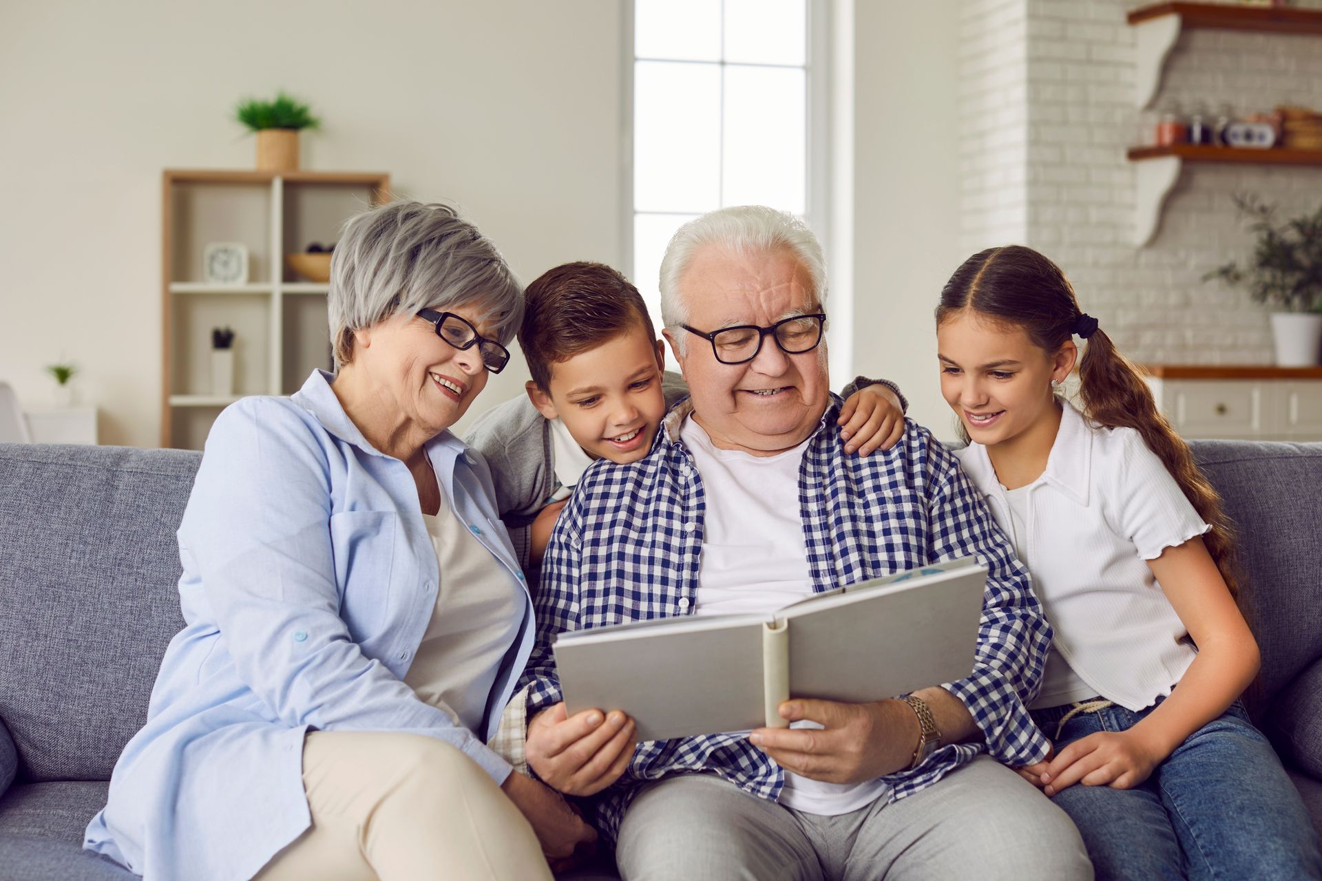 Grandparents show grandkids a photo album on a sofa in a living room.
