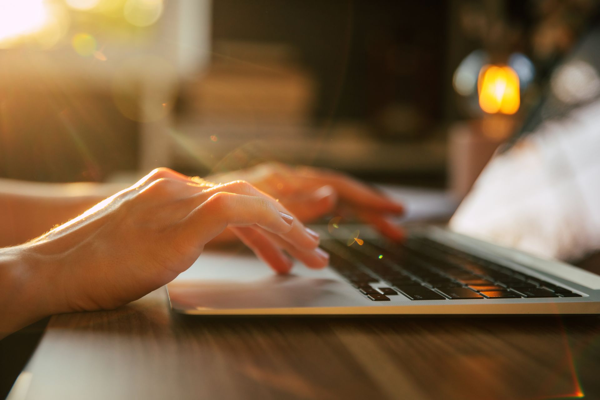 Hands typing on a laptop keyboard; warm sunlight in the background.