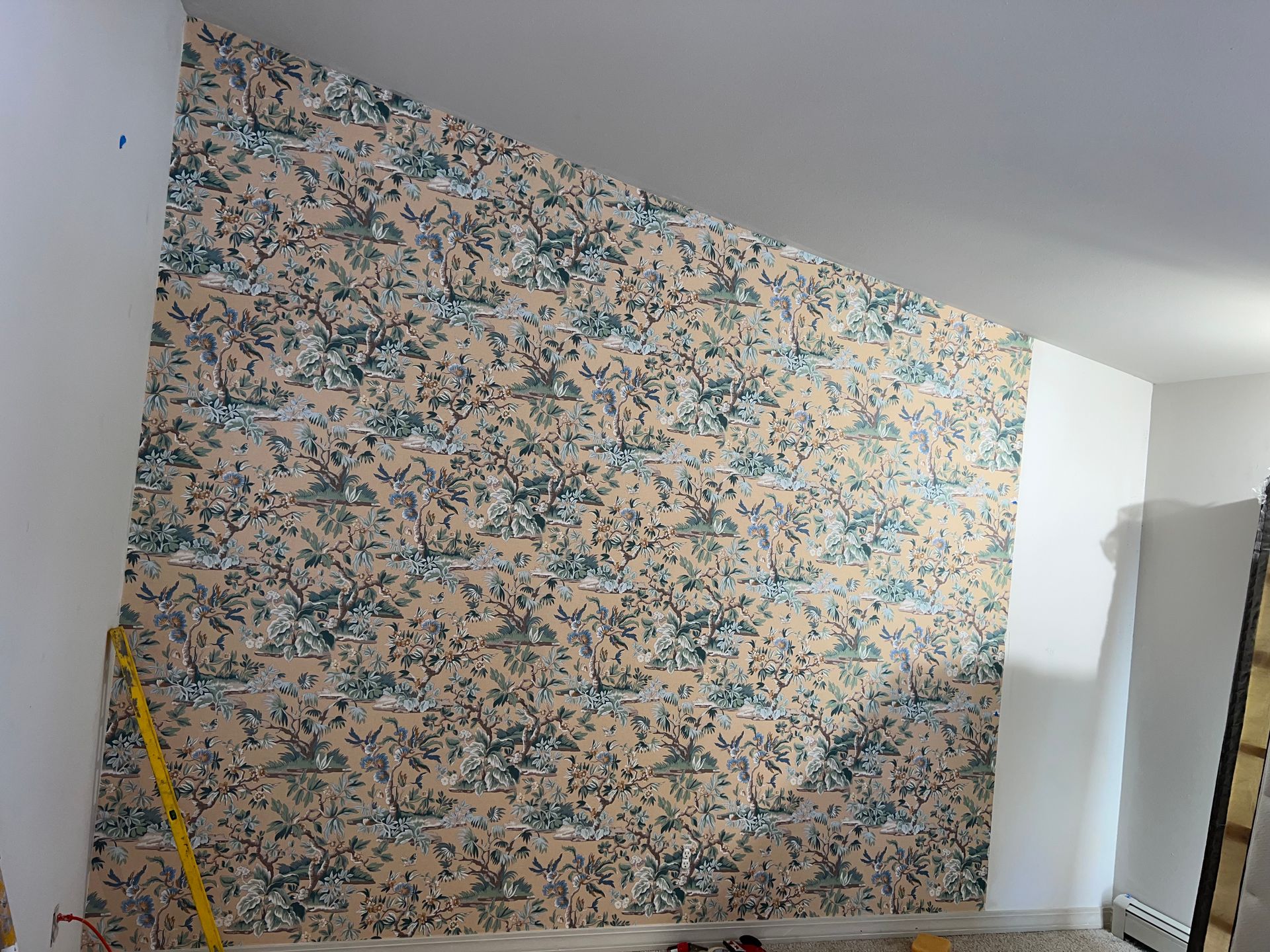 A room with a floral wallpaper on the wall and a yellow ruler on the floor.