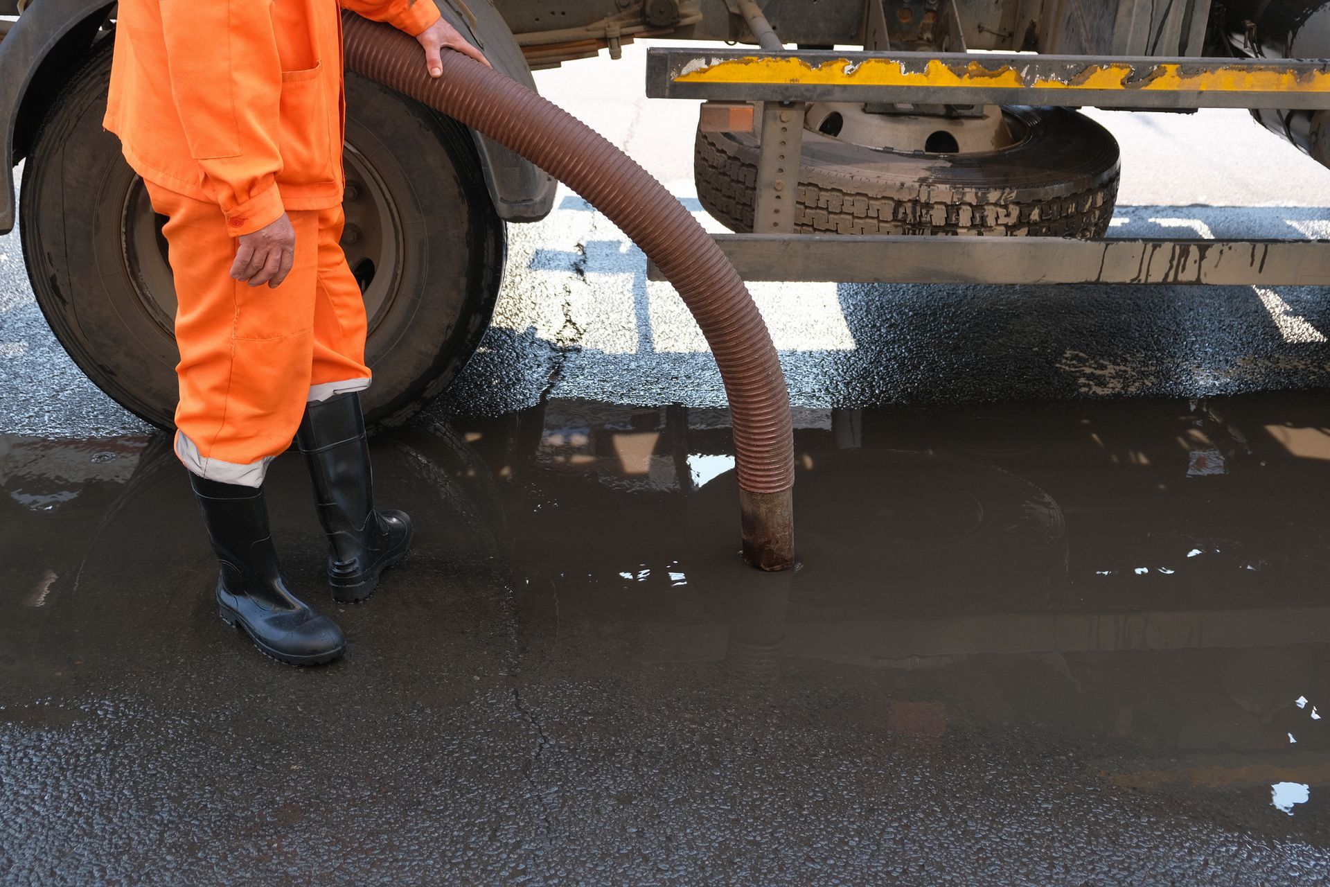Worker using vacuum hose for street sewer cleaning near a vacuum truck.