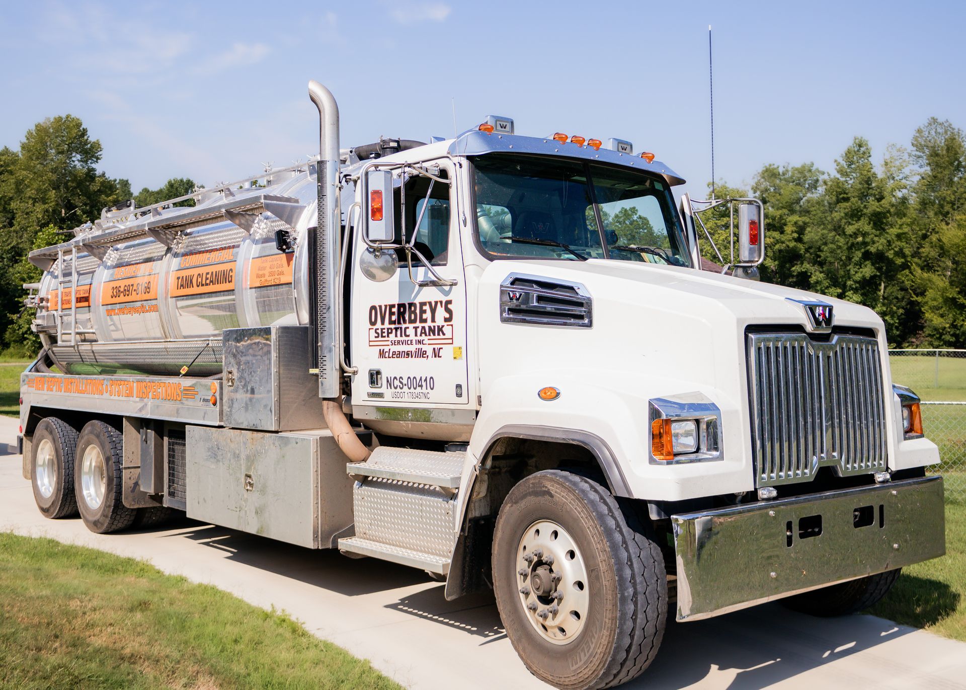 White septic truck parked on a driveway, logo visible: 