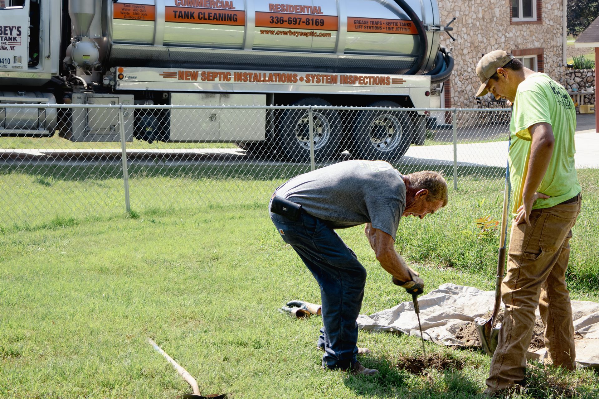 Two men working on a lawn, likely septic repair; truck in background.