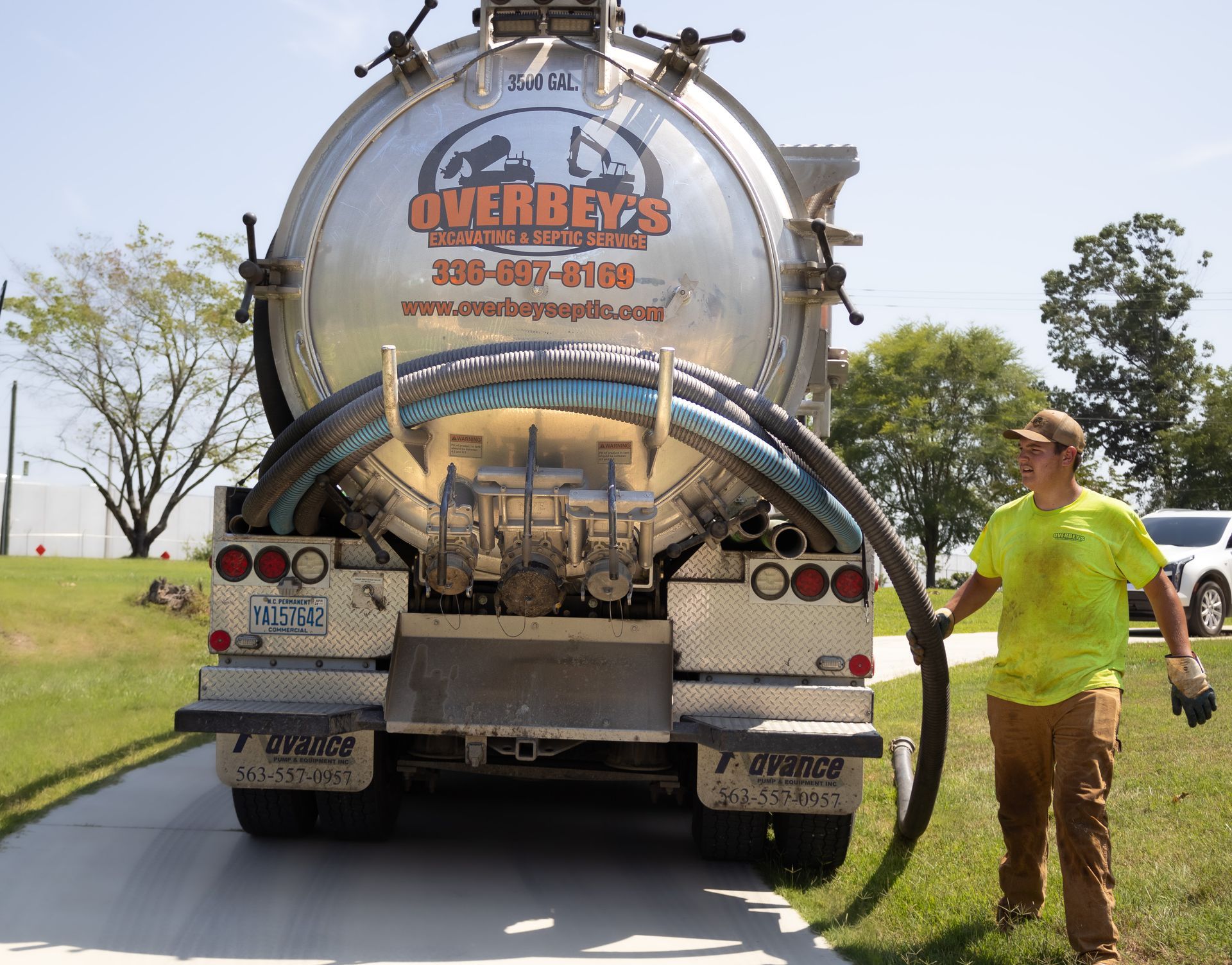 A septic tank truck with a worker holding a hose on a sunny day.