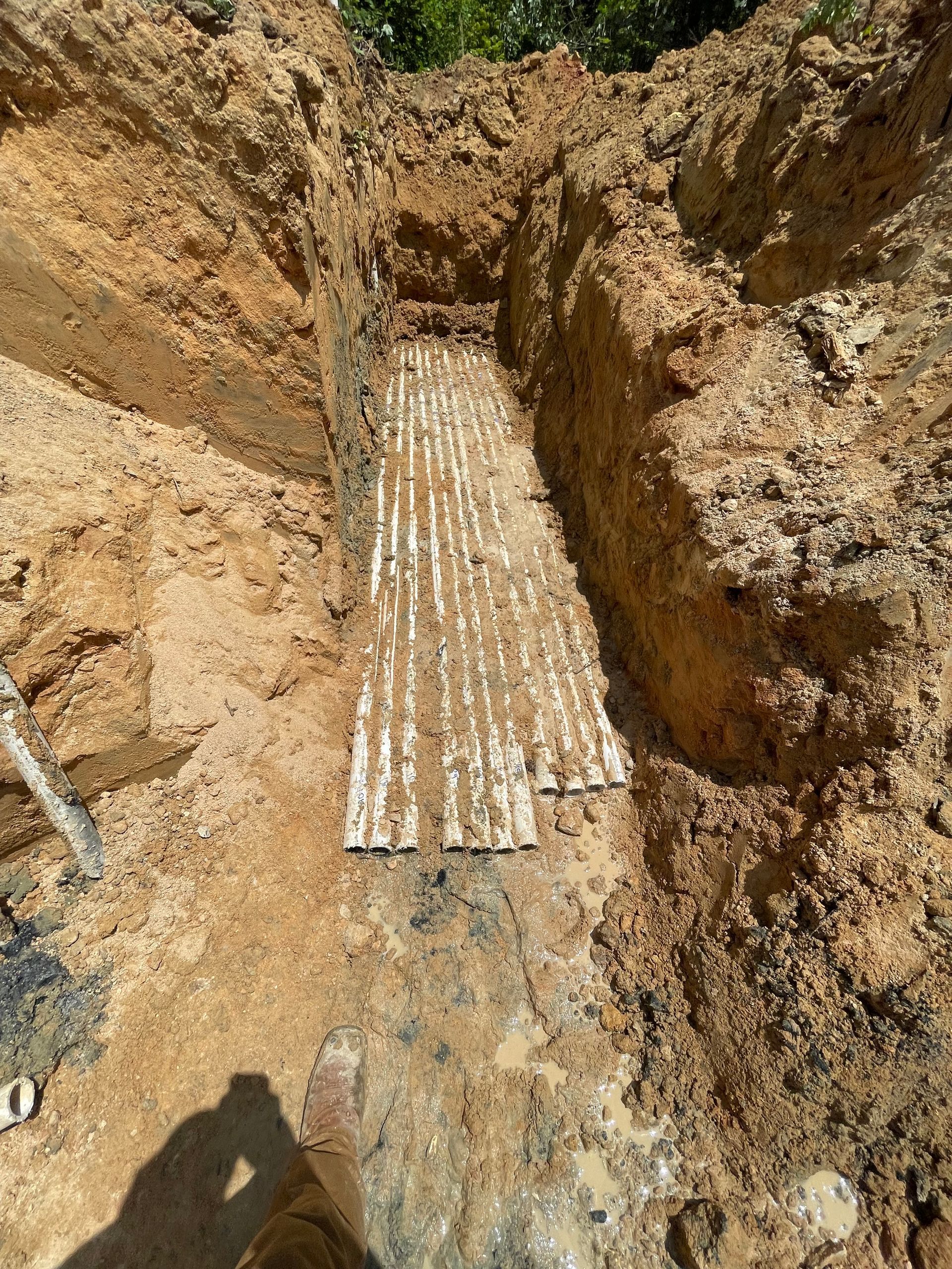 Trench in brown earth reveals buried white pipes, possibly for utilities, at a construction site.