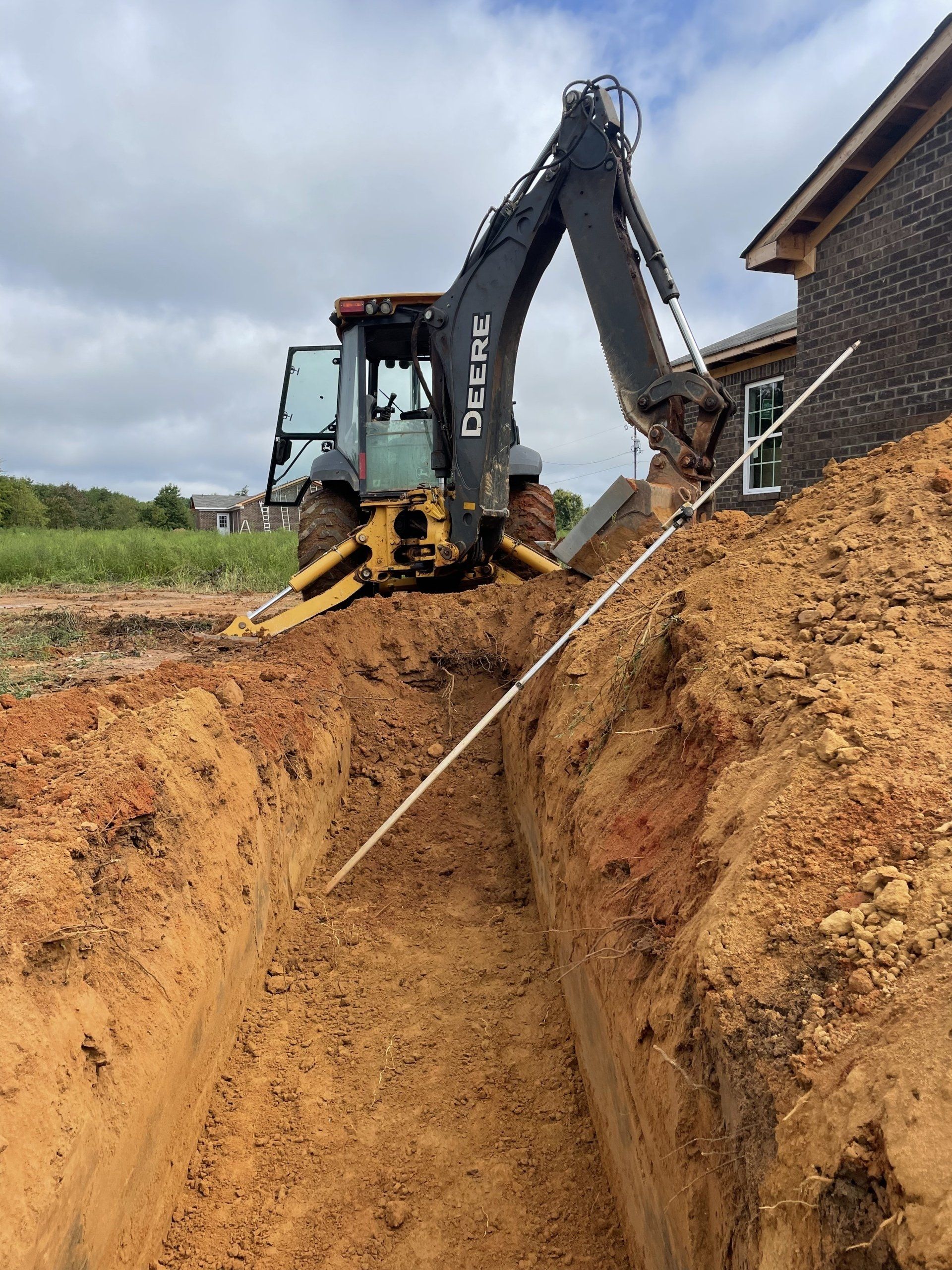 Backhoe digging a trench next to a house under construction, with the blue sky in the background.