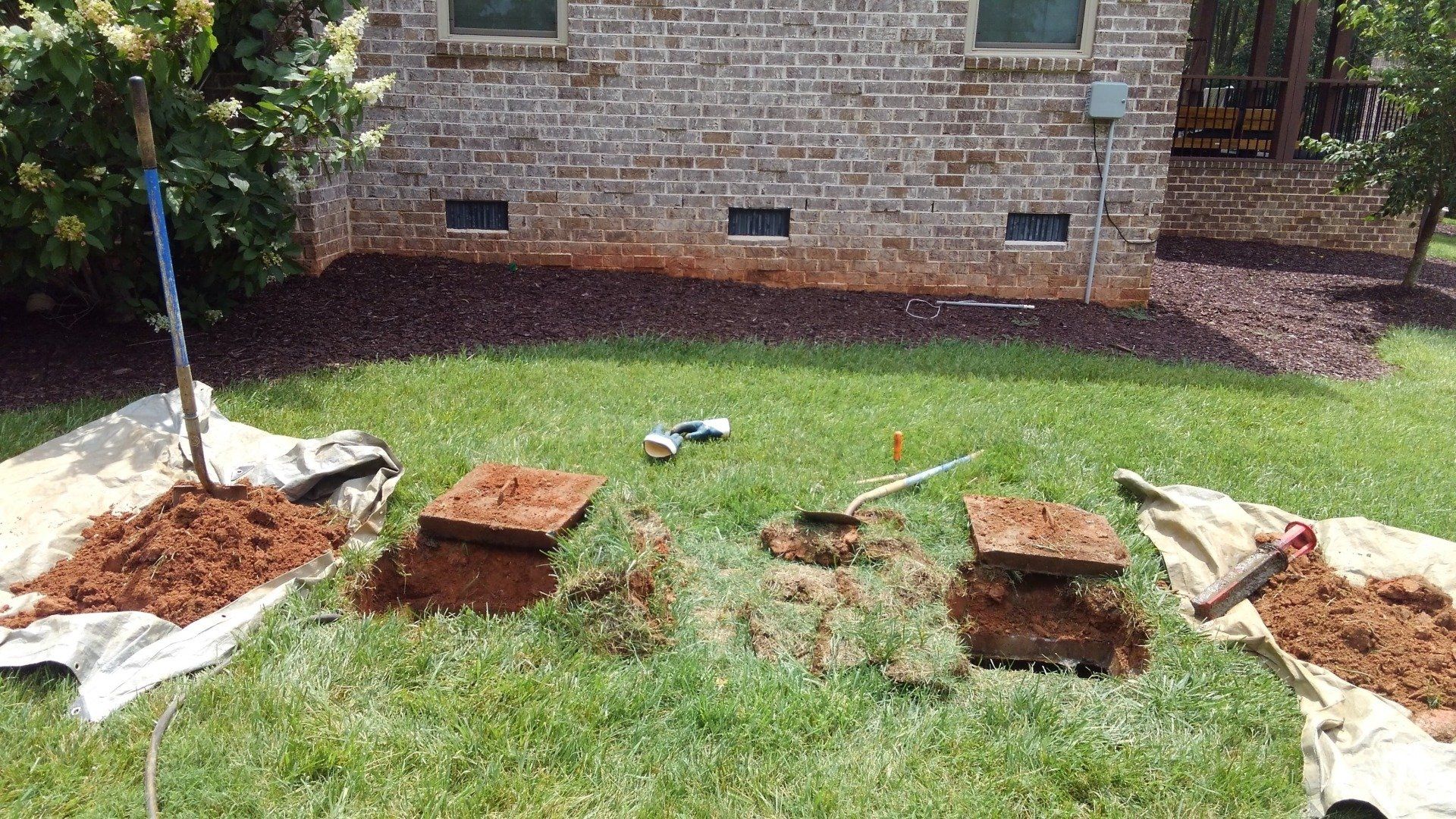 Lawn with three opened boxes, soil, tools, and a brick building in the background.
