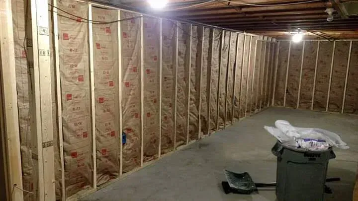 A basement with insulation on the walls and a trash can.